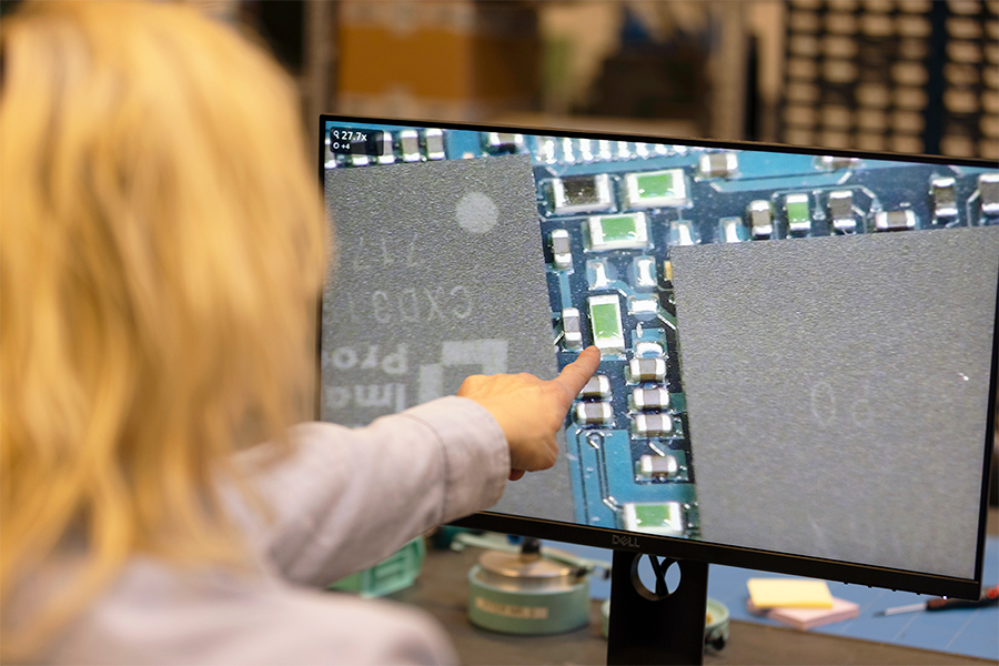 Operator pointing at a monitor showing a magnified PCB