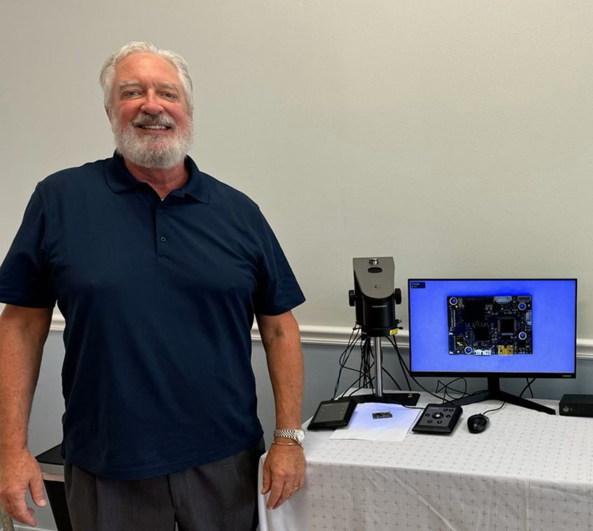 Mark Sullivan in a blue t-shirt and dark pants next to a table that displays the TAGARNO microscopes